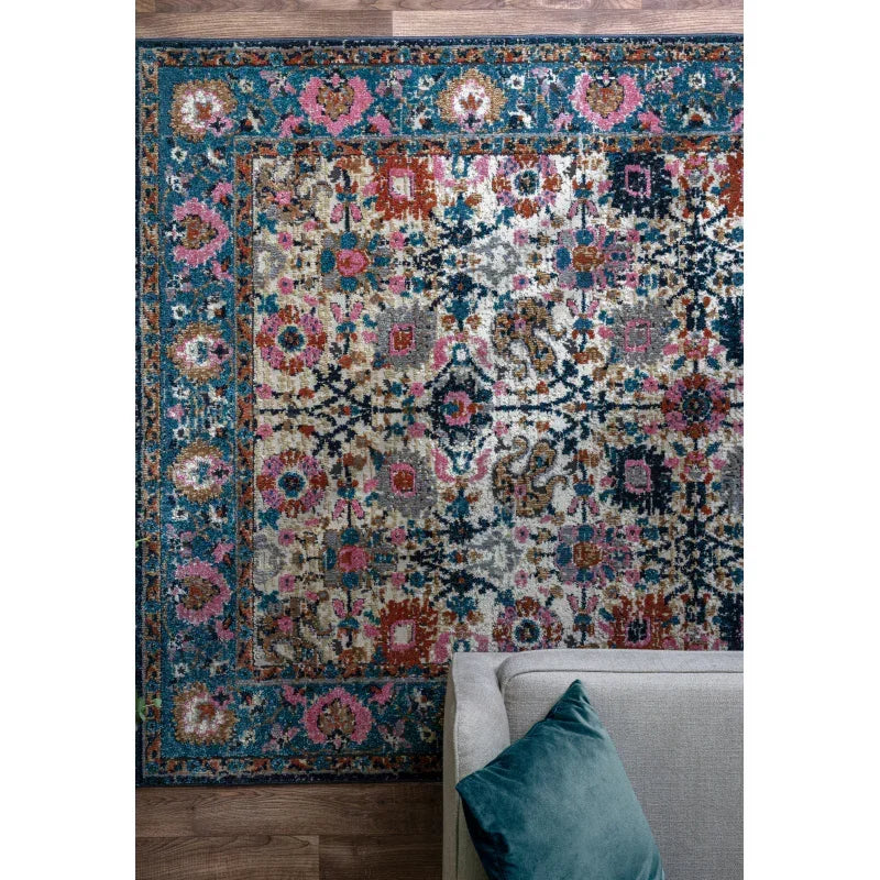 Patterned area rug with blue, pink, and cream accents beside grey sofa on wood floor
