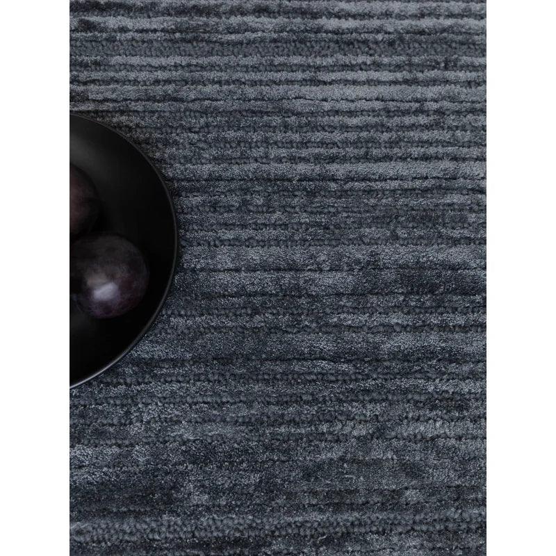Textured charcoal grey rug with bowl of dark plums on one corner