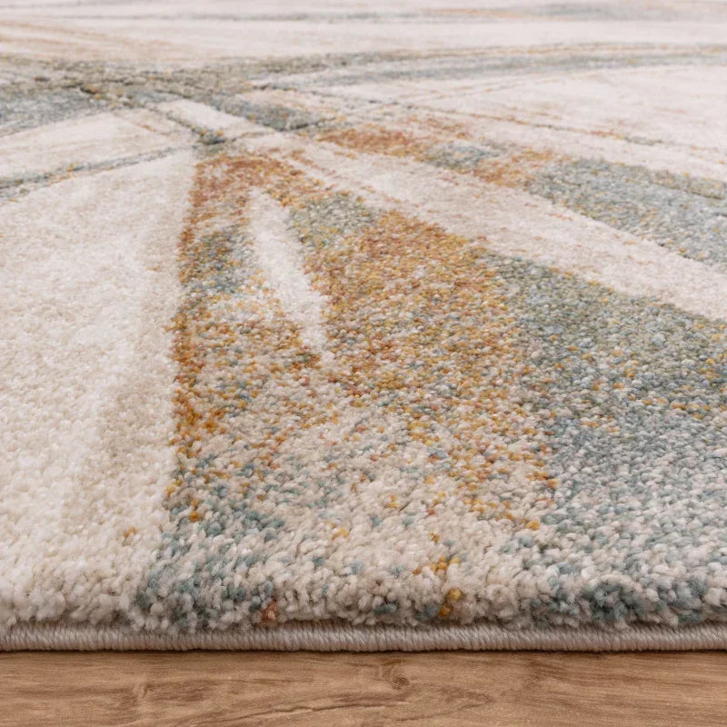 Modern abstract area rug with soft pile in beige, blue, and gold tones on wooden floor