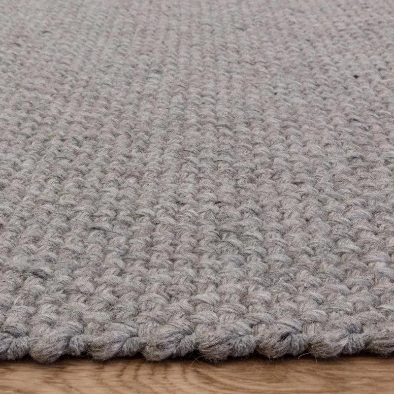 Grey woven wool rug with chunky texture on wooden floor, close-up edge view