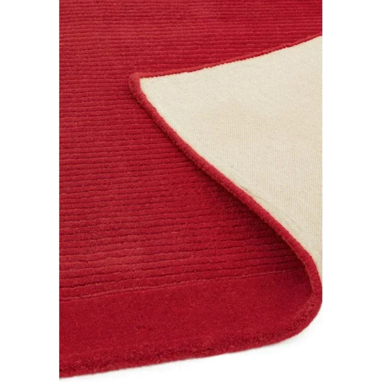 Red area rug with visible textured surface and corner flipped to show beige backing