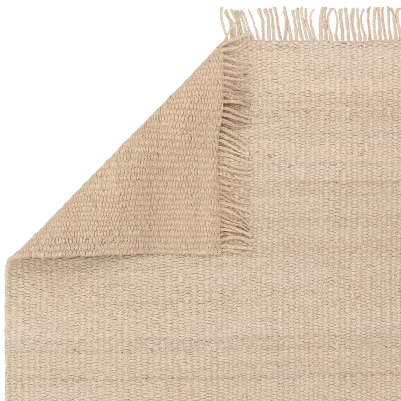 Beige jute rug with woven texture and fringe detail on corner