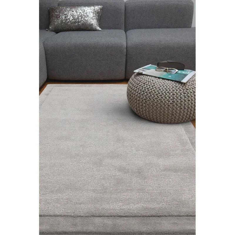Light grey area rug on wooden floor with grey sofa and knitted pouffe in living room
