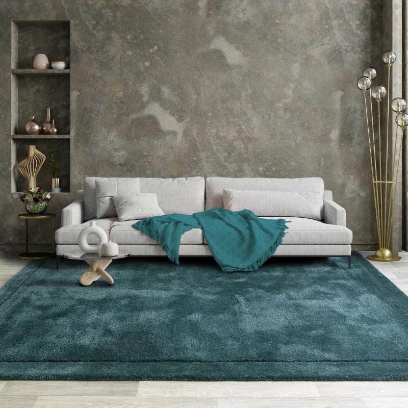 Grey fabric sofa with teal throw blanket on large teal rug in modern living room