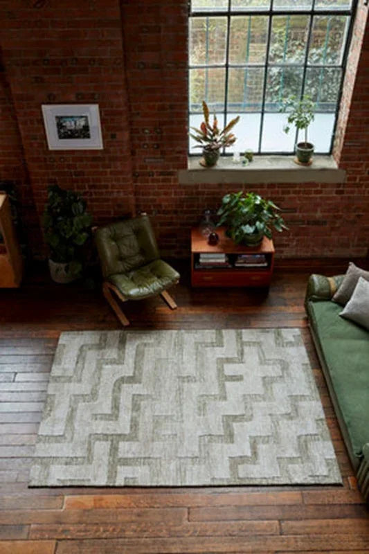 Geometric patterned area rug on wood floor in loft living room with green sofa and plants