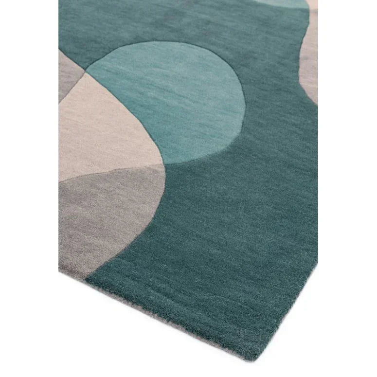 Geometric patterned area rug in teal, blue, and grey tones, viewed from the corner angle
