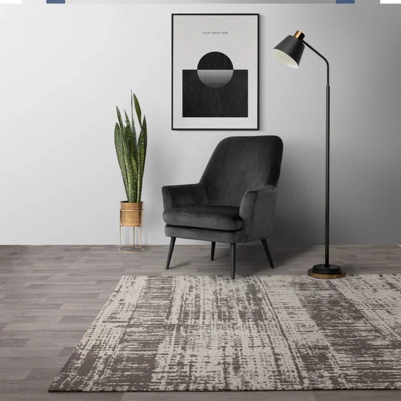 Modern grey accent chair with gold planter, floor lamp, abstract wall art and contemporary rug