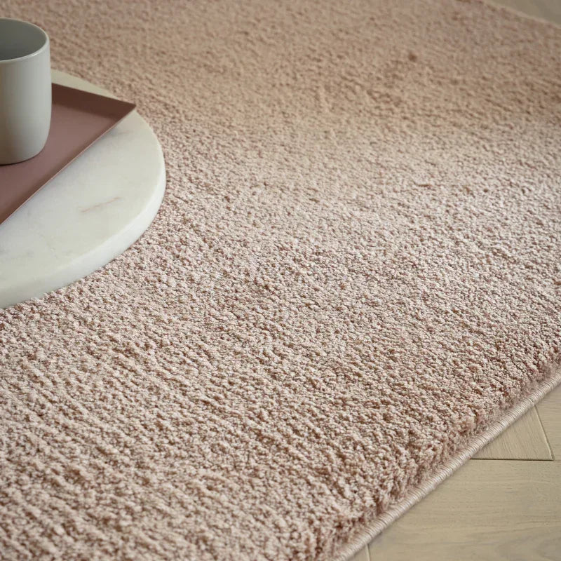 Blush pink textured rug on wooden floor with round marble tray and mug