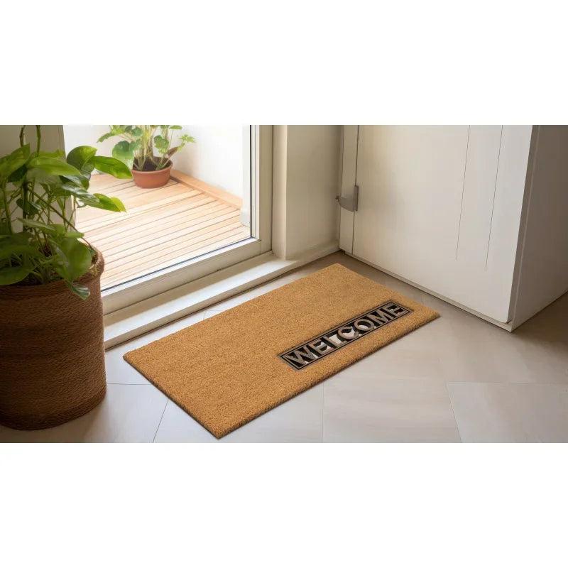 Coir welcome doormat placed at entrance beside indoor plant and glass door