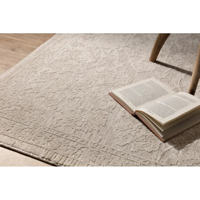 Beige textured rug with subtle pattern, open book, wooden chair leg on wood flooring