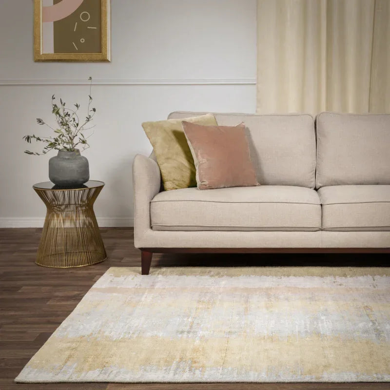 Beige fabric sofa with pink and green cushions, next to gold side table on wood flooring