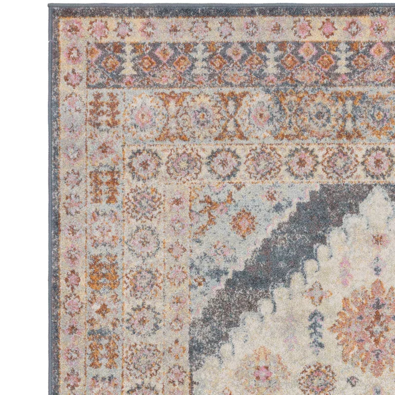 Corner of patterned area rug with muted blue, pink, and gold geometric and floral designs