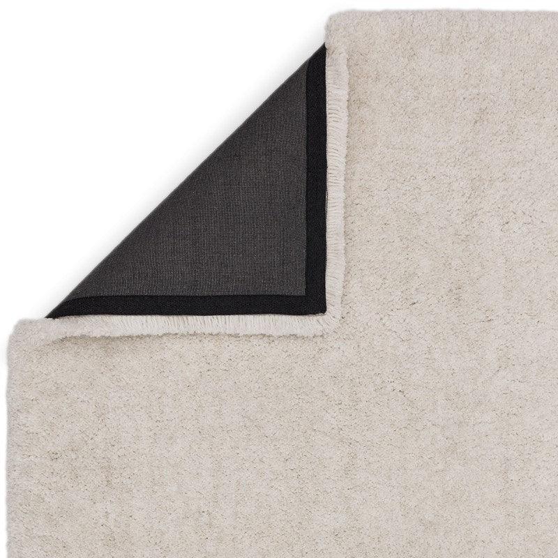 Beige shaggy rug with black anti-slip backing corner flipped up