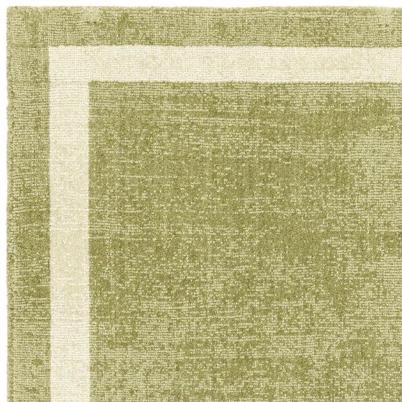 Close-up of green area rug with cream border and textured weave