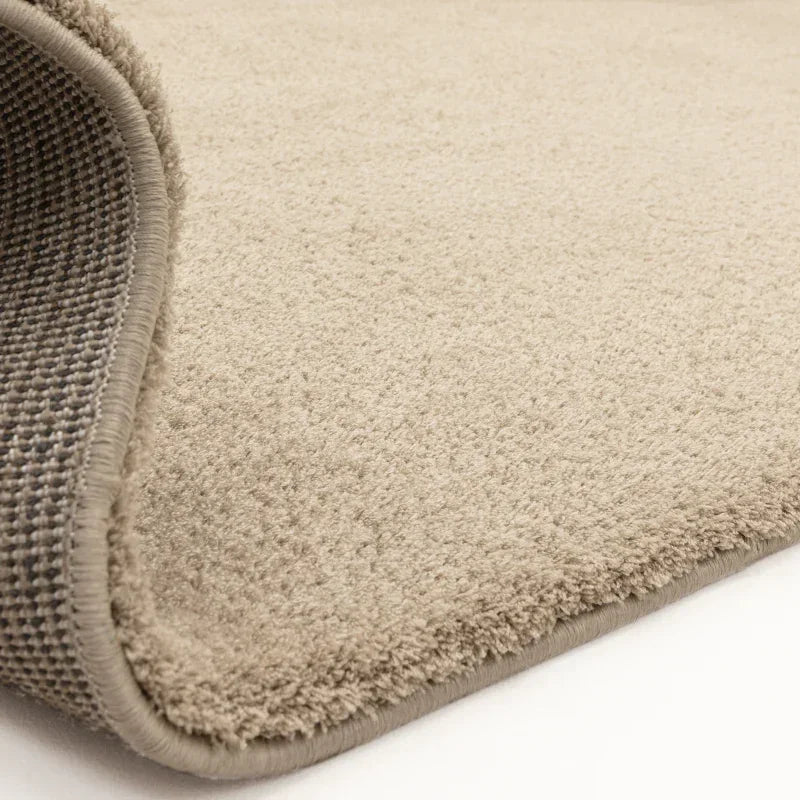 Beige carpet rug closeup showing textured pile and stitched edge with non-slip backing