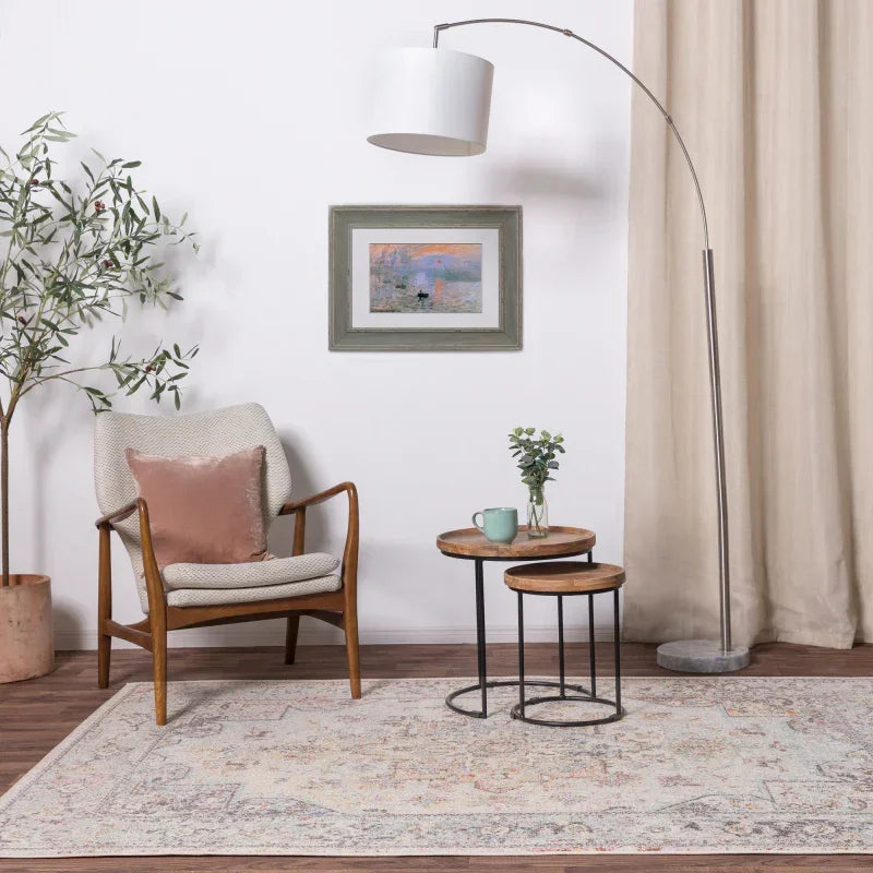 Modern armchair with blush cushion beside nested wood tables on patterned living room rug
