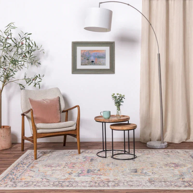 Scandi style armchair and nesting tables on patterned rug with arc floor lamp in living room