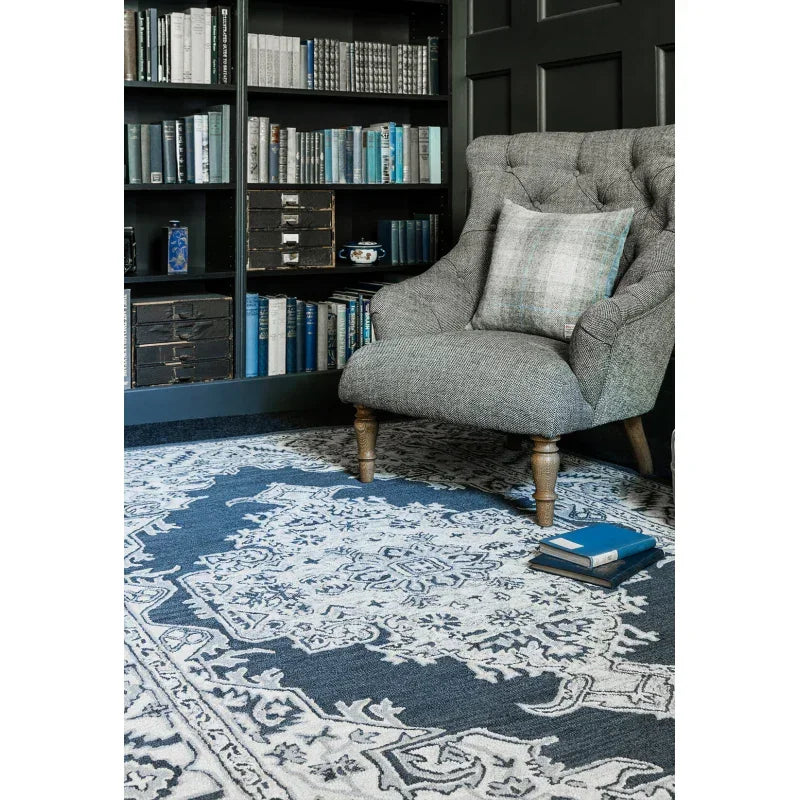 Grey armchair with plaid cushion on patterned rug in home library setting