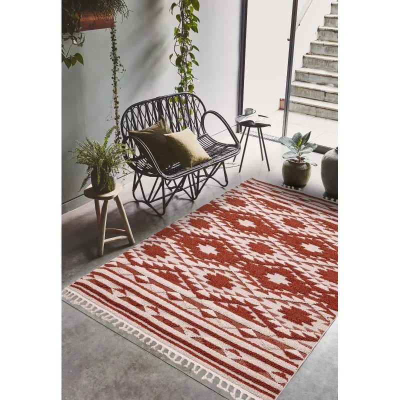Red and cream patterned area rug in modern living room with black rattan bench and plants