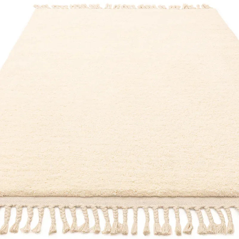 Cream area rug with tassel fringe, textured surface, close view of edge detail