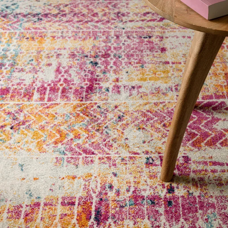 Multicoloured area rug with pink and yellow geometric pattern beside wooden table leg