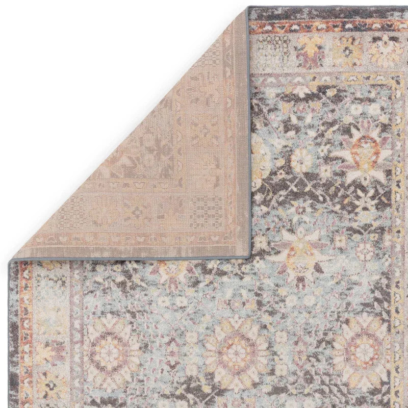 Floral patterned area rug with folded corner showing back and detailed border design