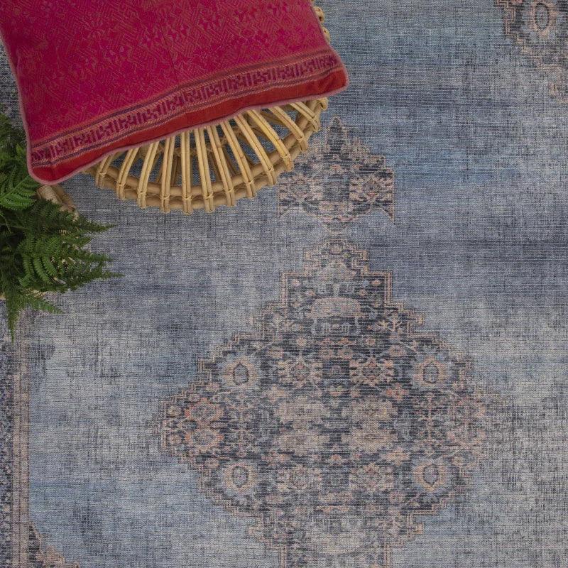 Blue patterned area rug with traditional design beside rattan stool and red cushion