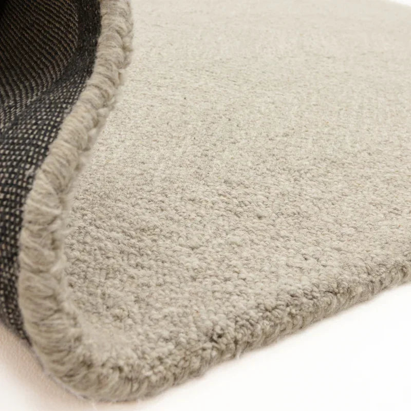 Closeup of beige wool rug with textured weave and stitched edge on light surface