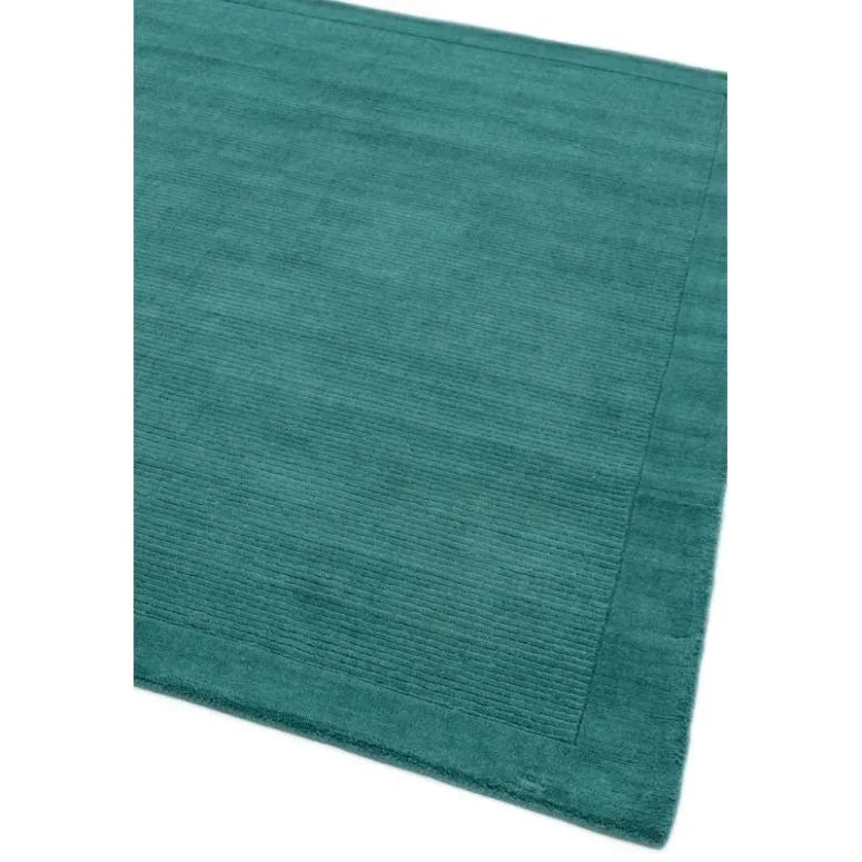 Teal wool rug with textured border and ribbed pattern, shown from a corner angle