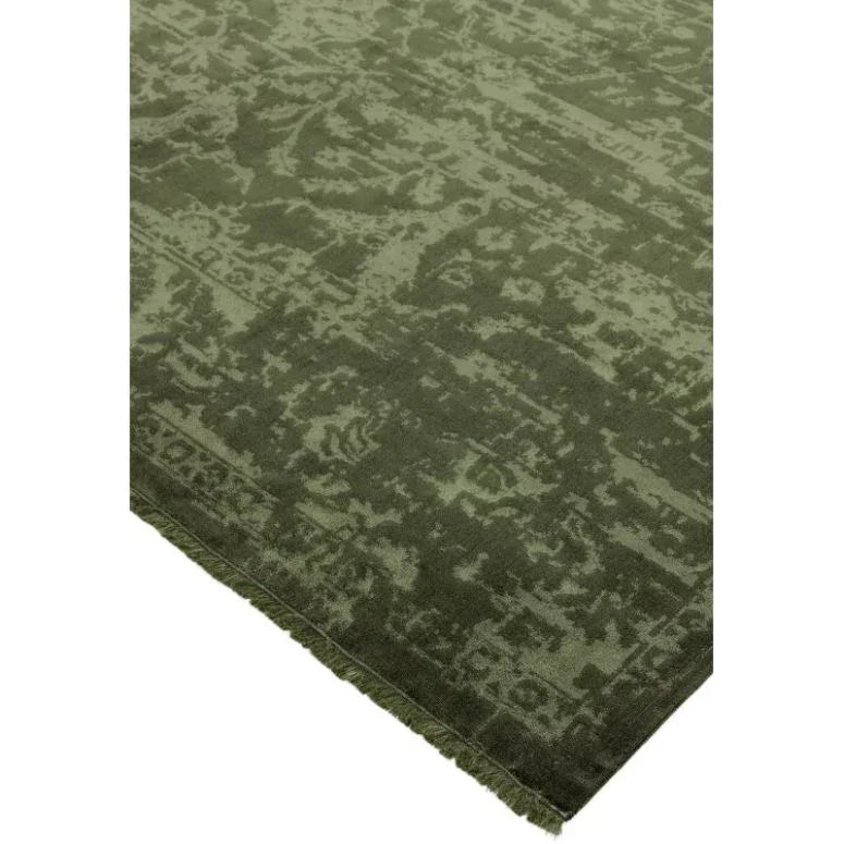 Green patterned area rug with subtle distressed design and fringed edge, corner view