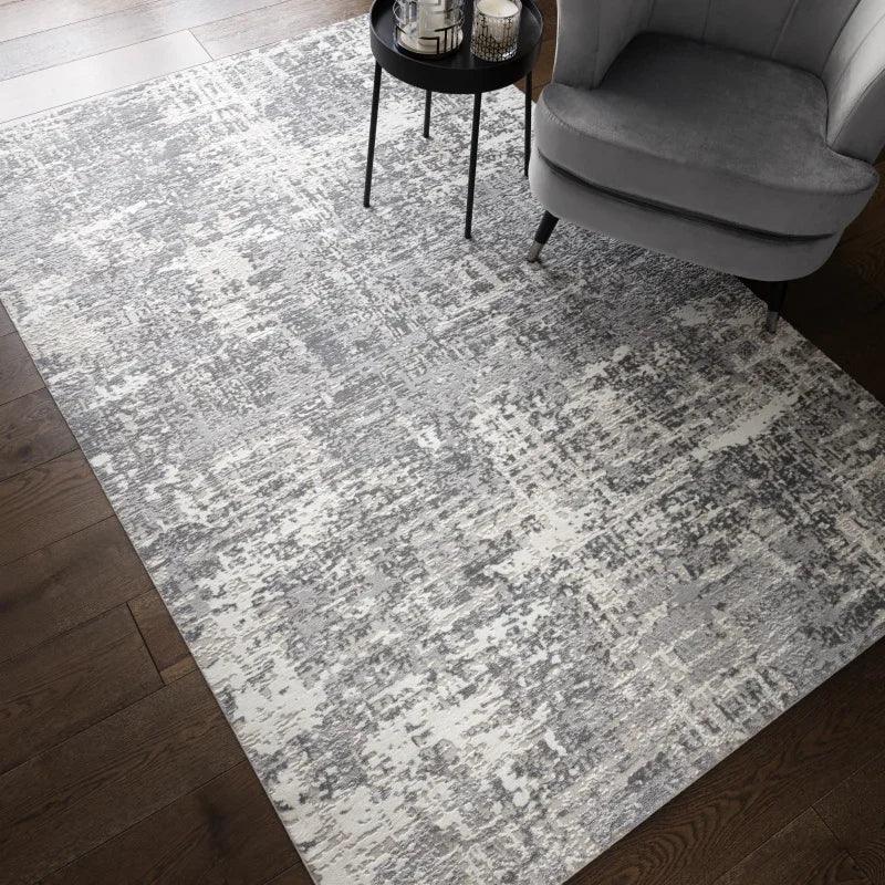 Grey and white abstract area rug on dark wood floor beside grey armchair and side table