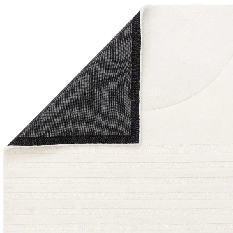 White textured rug with black trimmed corner folded to show reverse side
