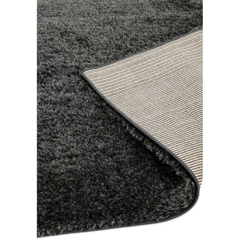 Black shaggy rug with soft pile, corner lifted to show backing material detail