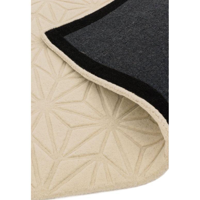 Cream geometric pattern rug with corner lifted showing black fabric backing