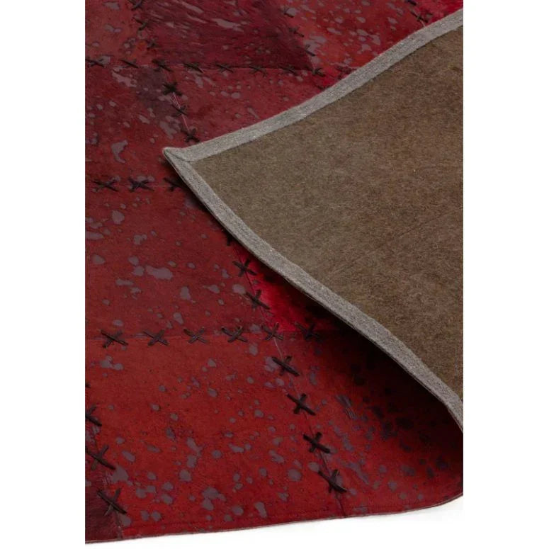 Red cowhide rug with cross-stitch detail and folded corner showing brown felt backing