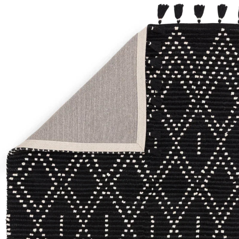 Black and white patterned area rug with tassels and corner fold showing backing