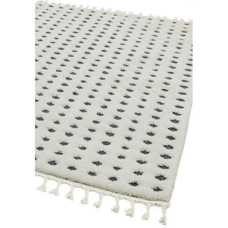 White patterned rug with black dotted design and tasseled edge, corner angle view