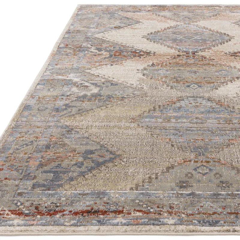 Neutral geometric area rug with faded blue, beige, and rust pattern, corner angle view
