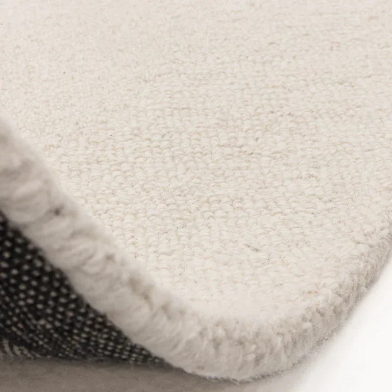 Close-up of cream wool rug corner showing textured loop pile and woven backing