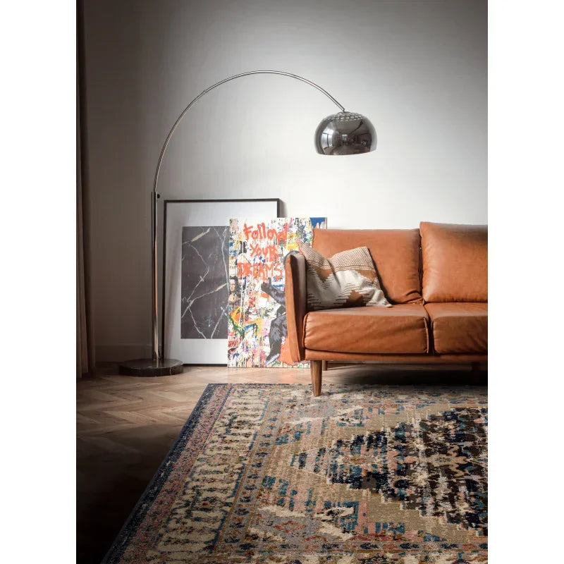 Brown leather sofa with patterned cushion beside arc floor lamp and abstract wall art