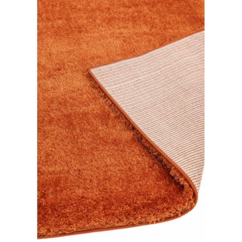 Closeup of orange shaggy rug with corner flipped to show non-slip backing