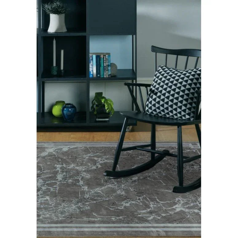 Grey marble pattern area rug on wooden floor with black rocking chair and geometric cushion