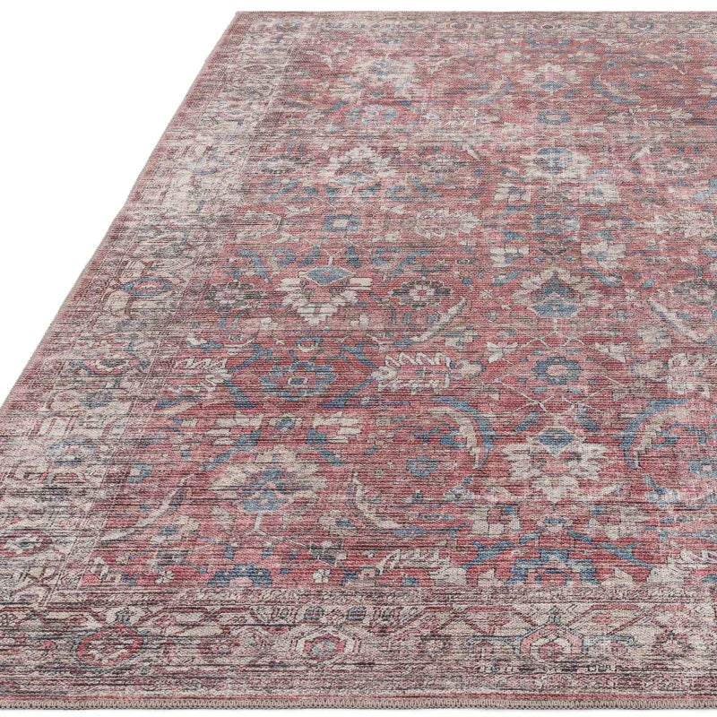 Rust red area rug with vintage floral pattern and blue accents, corner view on white background