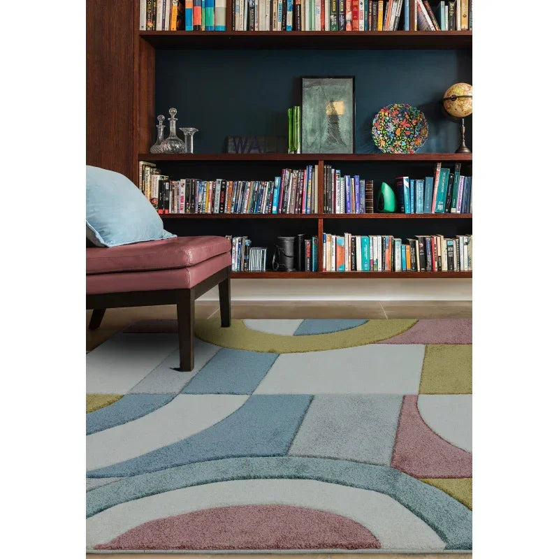 Geometric patterned rug in blue, green, and pink beside bookshelf and upholstered chair