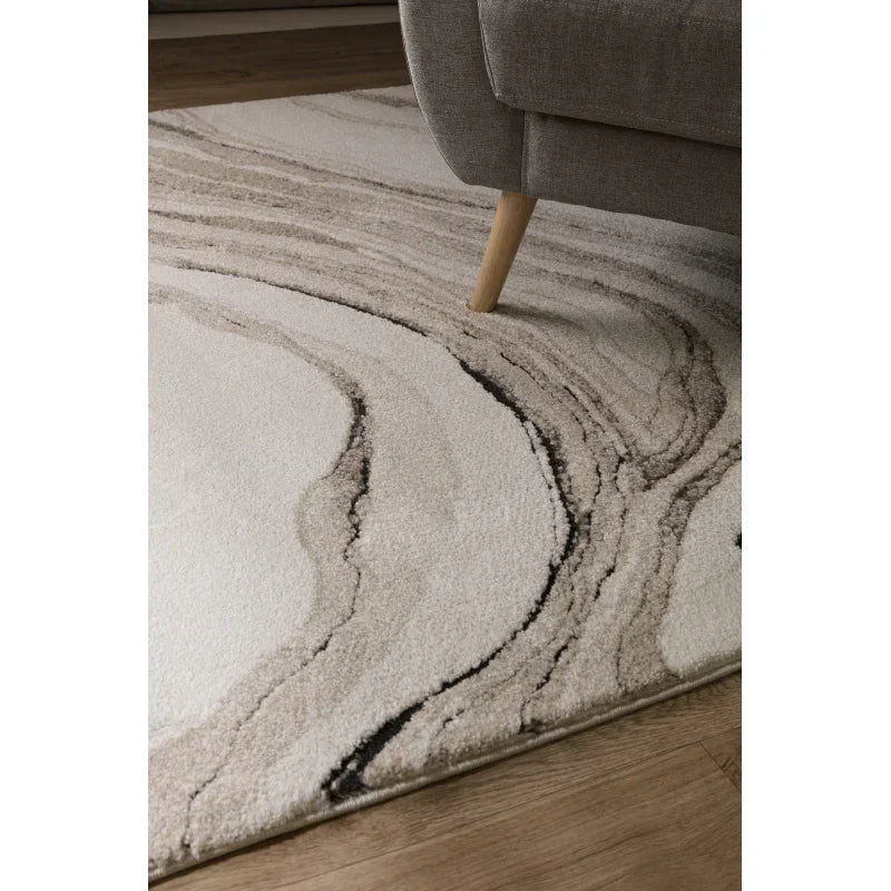 Modern beige and cream area rug with abstract swirl design beside grey sofa on wooden floor