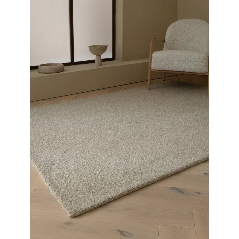 Beige textured area rug on light wooden floor with modern accent chair in neutral living room