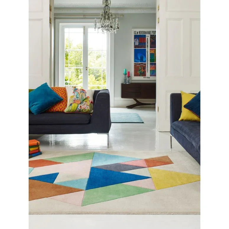 Geometric multicolour rug on white floor between navy sofas with bright cushions in modern living room