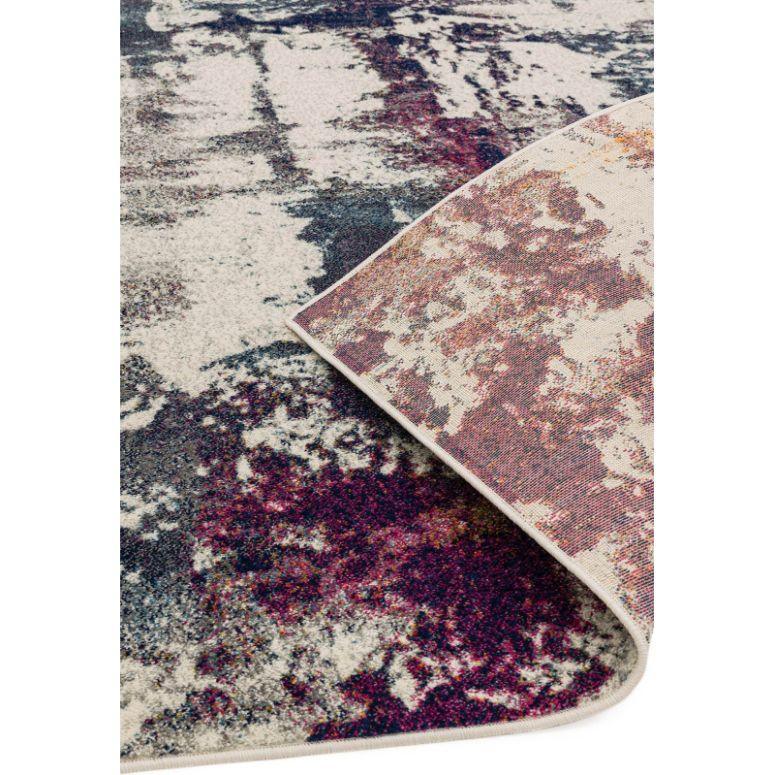 Abstract patterned area rug in cream, navy, and purple with corner folded to show backing