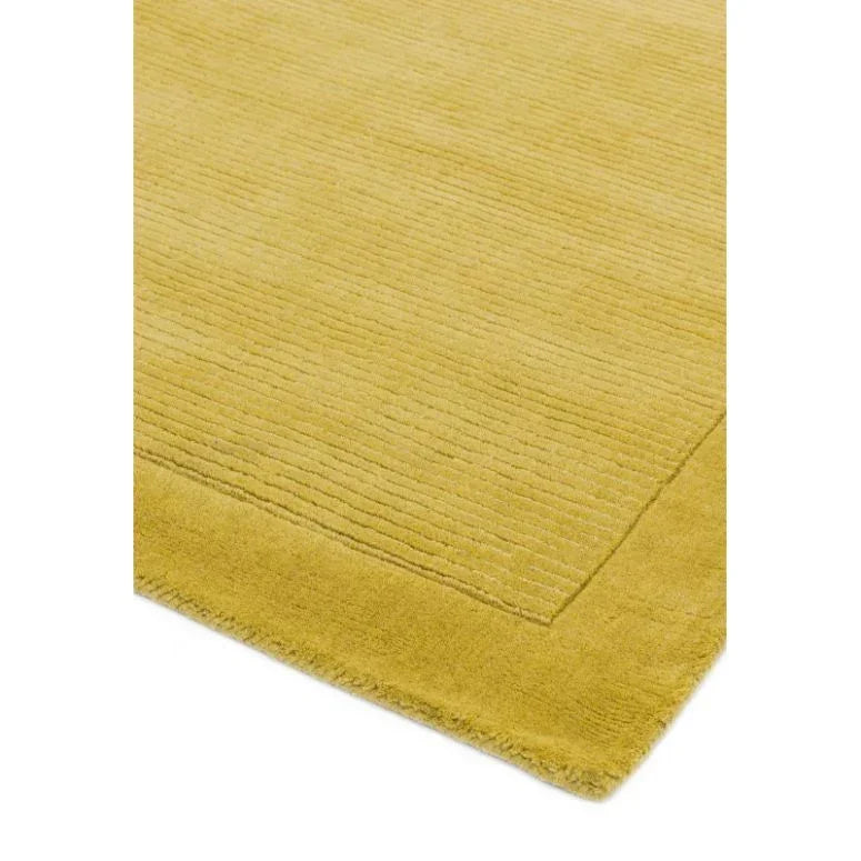 Mustard yellow rug with textured linear pattern and solid border, corner detail closeup
