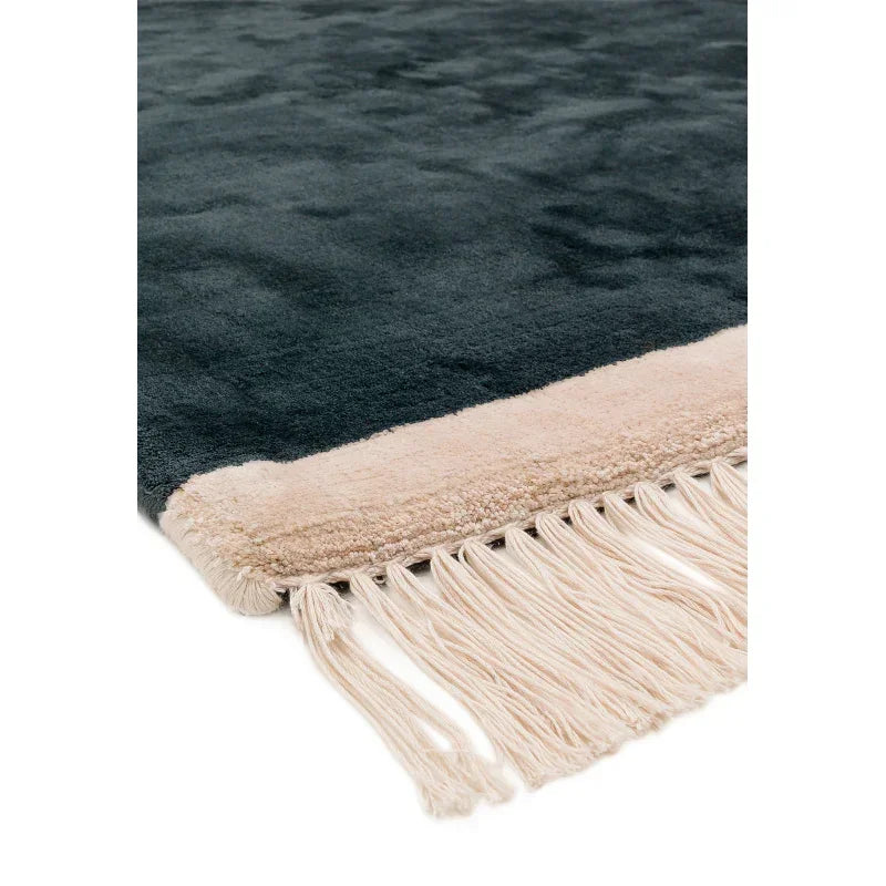 Closeup of dark green area rug with beige border and fringed edge detail